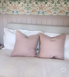 two pink pillows sitting on top of a bed next to a wallpapered headboard