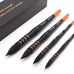 four pens are lined up in front of a black box with orange trimmings