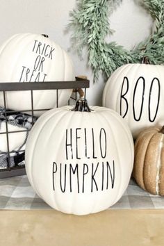 three white pumpkins with handwritten words on them sitting on a shelf next to a wreath