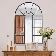 a vase with flowers on top of a wooden dresser next to a mirror and window