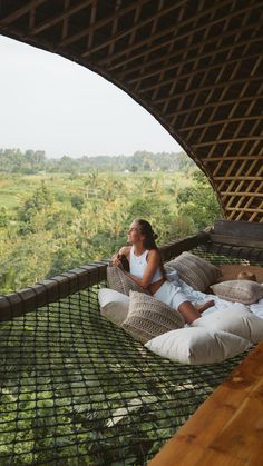 a woman sitting in a hammock on top of a lush green field with trees