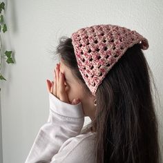 a woman wearing a pink crocheted hat covering her face with her right hand