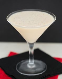 a drink in a martini glass sitting on a red and black place mat with a napkin