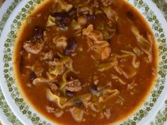 a bowl filled with meat and vegetable soup on top of a green and white plate