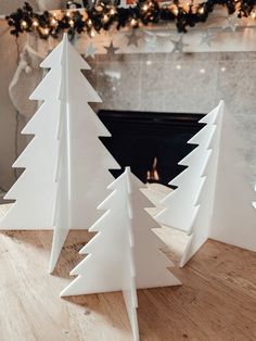 three white christmas trees sitting on top of a wooden table next to a fire place