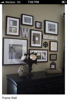 a black dresser topped with a vase filled with flowers next to pictures on the wall