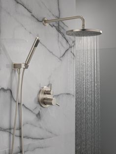 a shower head with thermostaer and hand held shower faucet in front of marble wall