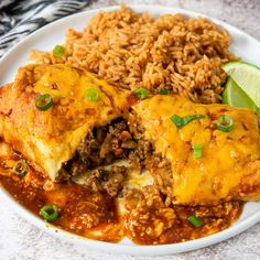 a white plate topped with enchiladas and rice next to a slice of lime