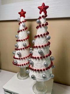 two white christmas trees with red and silver balls on them sitting on a counter top