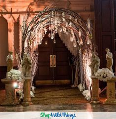 an archway decorated with white flowers and branches in front of a building entrance at night