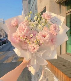 a bouquet of pink and white flowers is being held by someone's hand on the sidewalk