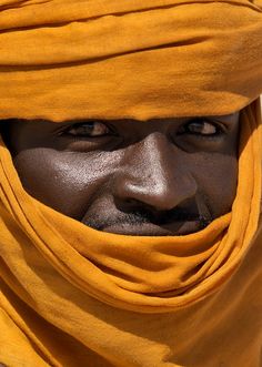 a man wearing a yellow head scarf and looking at the camera with an intense look on his face