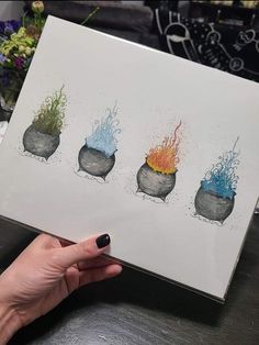 a hand holding up a drawing of three pots with fire and water in them, on top of a table