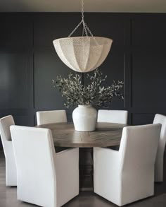 a dining room table with white chairs and a round wooden table surrounded by black walls