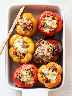 several stuffed peppers in a casserole dish with a wooden spoon on the side