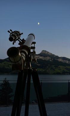 a telescope on a tripod with the moon in the sky behind it and mountains in the background