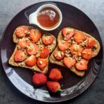 two pieces of toast on a plate with strawberries next to it and a cup of tea