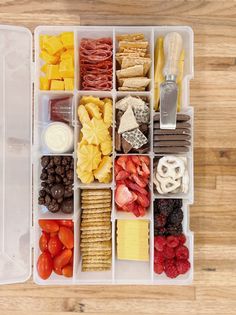 a plastic container filled with lots of different types of food and snacks on top of a wooden table