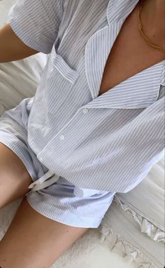 a woman laying on top of a bed wearing short shorts and a button up shirt