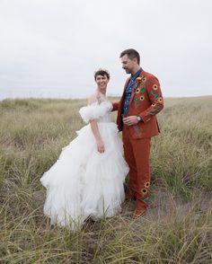 a man and woman in wedding attire standing together on the grass with tall grasses behind them