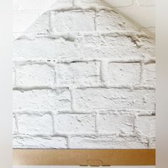 a white brick wall with a brown cardboard box on it's bottom and an empty piece of wood in the middle