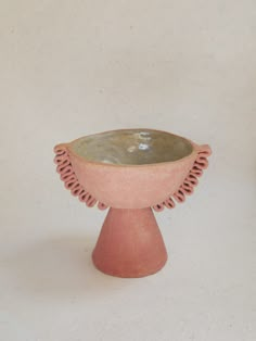 a small pink vase sitting on top of a white table next to a green planter