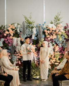 a man and woman standing next to each other in front of a floral wall with flowers