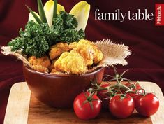 a wooden bowl filled with lots of food on top of a table next to tomatoes