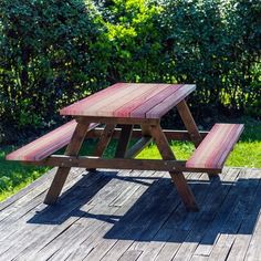 a wooden picnic table sitting on top of a wooden deck in front of some bushes