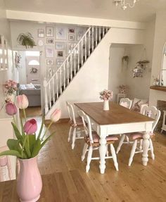 a dining room table and chairs with pink flowers in the vase on the wooden floor