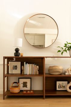 a shelf with books, pictures and a mirror on it in a room that has white walls