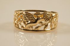 9ct engraved hummingbird yellow gold band The Hummingbird Ring symbolizes style, freedom, and a passionate spirit.  The hummingbird is a messenger of joy. It symbolizes intellect, beauty, devotion, and love.  Hummingbirds are a symbol of good luck. If you love fabulous nature-inspired bands, this is a lovely choice! This is just perfect - look at the hummingbird eating nectar out of the flower in this ring.  It is stamped 9ct and the ring is 10mm wide in the front and 3.7mm at the back for a com Hummingbird Ring, Precious Rings, Hummingbirds, Gold Band, Glasses Accessories, Rings Statement, Gold Bands, Nature Inspired, Statement Rings