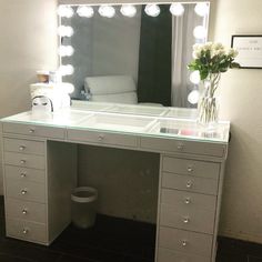 a white vanity with lights on it and a vase filled with flowers in front of the mirror