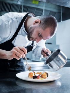 a man in an apron is preparing food on a white plate with a silver spoon