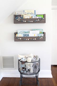 two wooden shelves holding books and stuffed animals in a wire basket on a wood floor