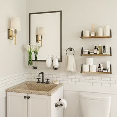 a white toilet sitting next to a sink in a bathroom under a mirror and shelves