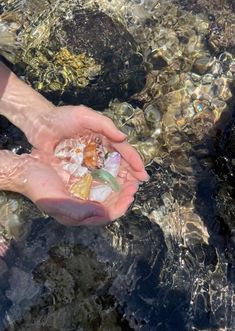 a person holding something in their hand while standing in some clear, crystal water on the beach