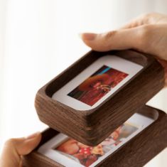 two wooden frames held in the air by one person's hand and another holding an open photo frame