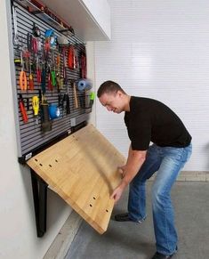 a man is holding a board with tools on it in front of a wall mounted tool rack