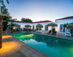 an outdoor swimming pool with lounge chairs and palm trees in the background at night time