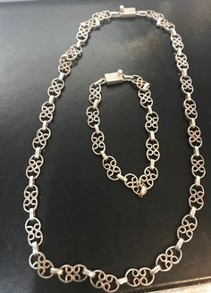 a silver necklace on a black surface with an open link and two smaller links in the middle