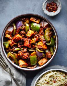 a bowl filled with stir fry vegetables next to a plate of noodles and a fork