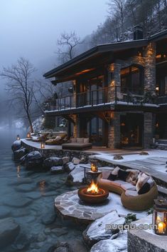 an outdoor fire pit in front of a large house on the water's edge