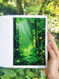 a person holding up an open book in front of trees and bushes with sunlight shining through the leaves