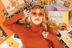 a woman in an orange turtle neck sweater and sunglasses with her hands on her head