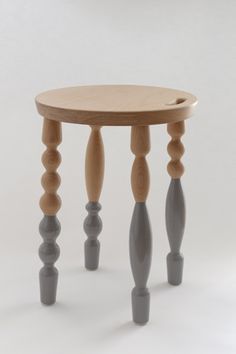 a small wooden table with three legs and two knobs on the top, sitting in front of a white wall