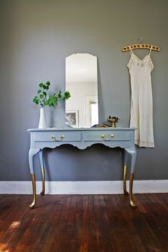 a blue table with gold legs and a mirror on it in front of a gray wall