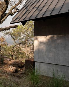 a small building with a metal roof next to a tree and rocks on the ground