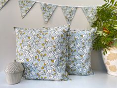 two blue and white pillows sitting on top of a table next to a potted plant