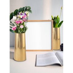 two gold vases with flowers in them and an open book next to it on a table